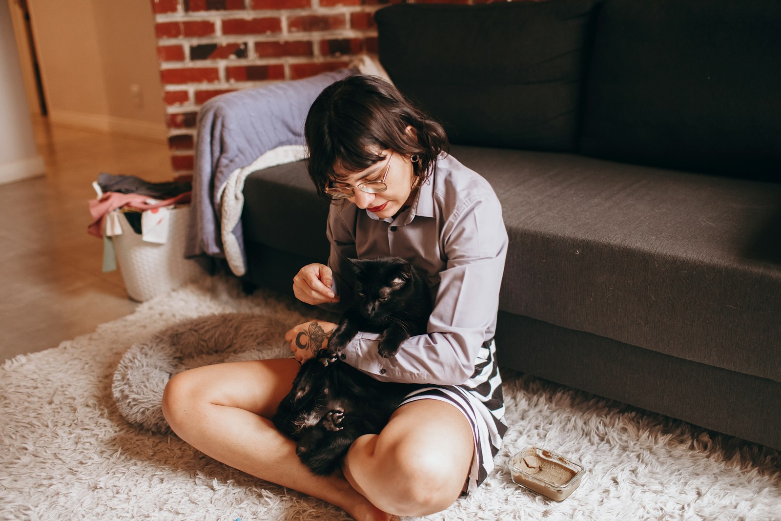 woman in white shirt and black shorts sitting on floor beside black cat, renters